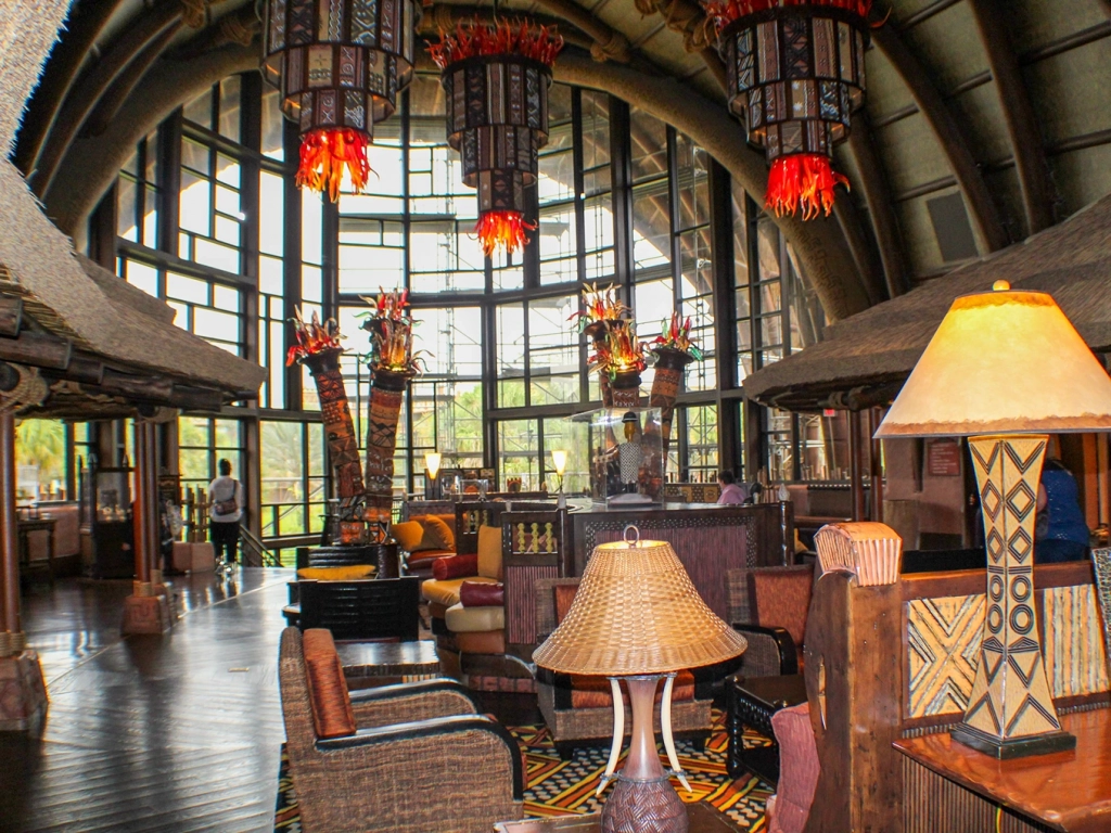 A spacious lobby at Disney's Animal Kingdom with large windows, vibrant decor, wooden furniture, and unique chandeliers.