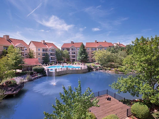 A peaceful view of Wyndham Branson at The Meadows by a pond with a fountain and a swimming pool.