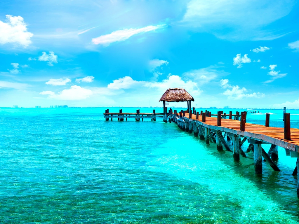 Wooden pier with a thatched-roof palapa extending into the turquoise ocean water of Cancun.