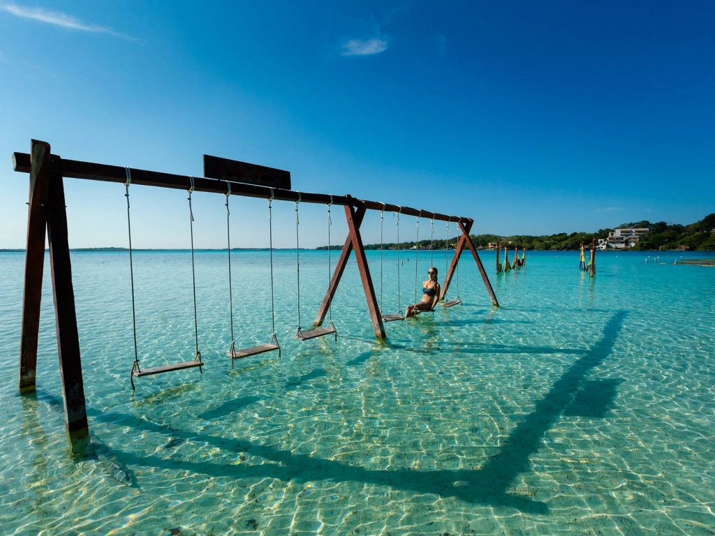 A woman relaxes on a wooden swing set built over shallow, clear turquoise water in Cancun.