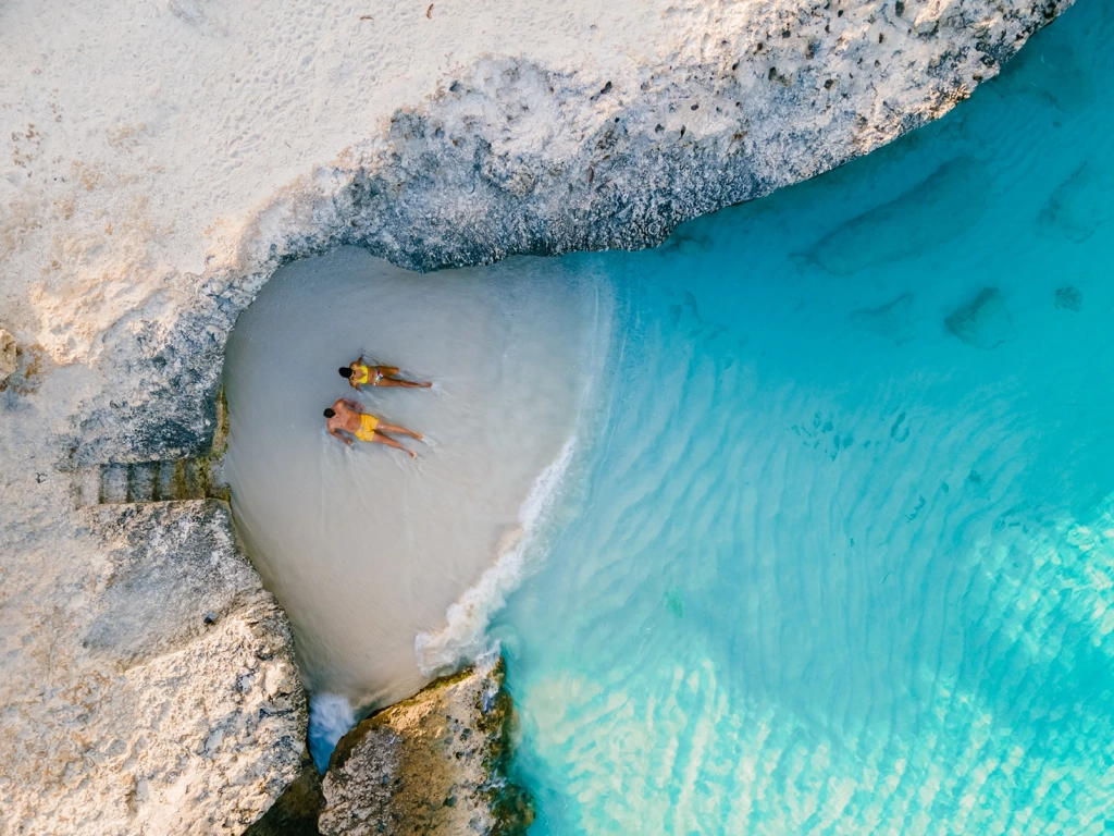 A woman relaxes on a wooden swing set built over shallow, clear turquoise water in Cancun.
