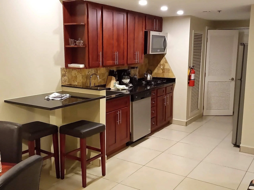 Fully equipped resort kitchen at Divi Village Golf and Beach Resort featuring dark wood cabinetry, black granite countertops, and a breakfast bar with stools.
