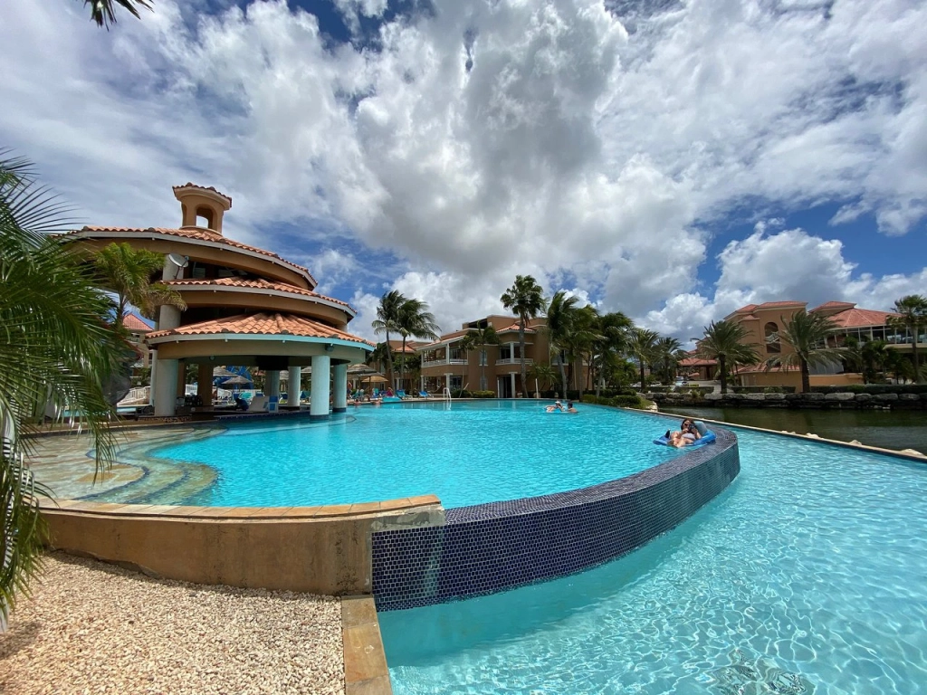 Wide view of a large swimming pool and circular swim-up bar pavilion at Divi Village Golf and Beach Resort in Aruba.
