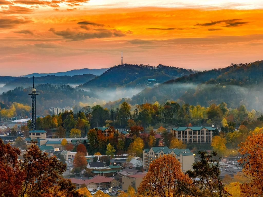 Misty sunrise over Gatlinburg, Tennessee, showing the Space Needle and mountains framed by colorful autumn foliage.