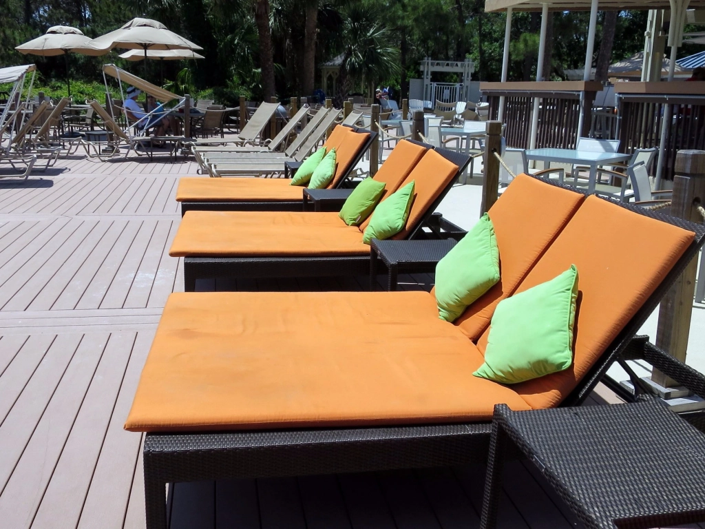 Poolside lounge chairs with orange cushions and green pillows on a wooden deck at Marriott's Grande Ocean. - Summer Vacation Ideas