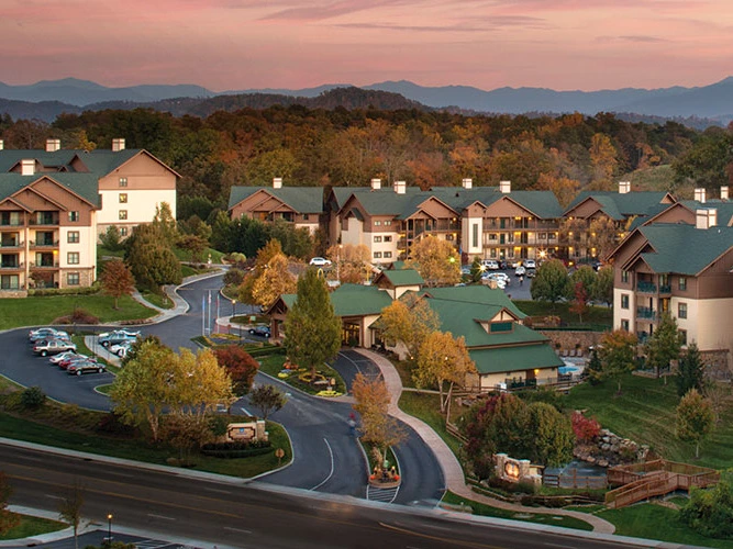 A scenic view of Wyndham Smoky Mountain Resort, surrounded by trees and mountains at sunset.