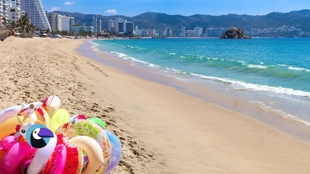 Unicorn pool floats on a sandy Acapulco beach with high-rise resorts and a rocky ocean island.