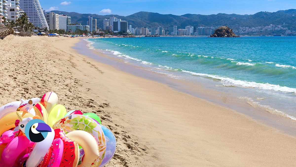Unicorn pool floats on a sandy Acapulco beach with high-rise resorts and a rocky ocean island.