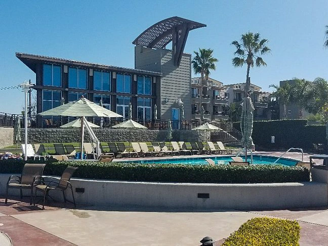 A swimming pool surrounded by lounge chairs and umbrellas, with palm trees and Carlsbad Seapointe Resort in the background.
