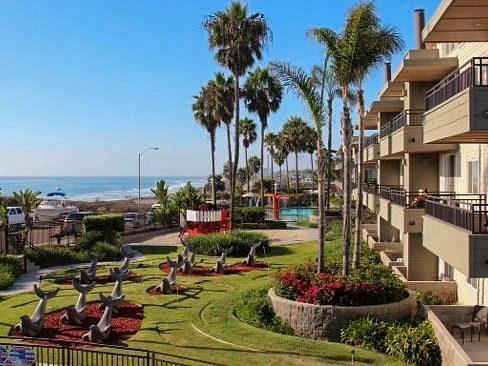 Carlsbad Seapointe Resort, with palm trees, a pool, and sculptures of whales in a green garden.