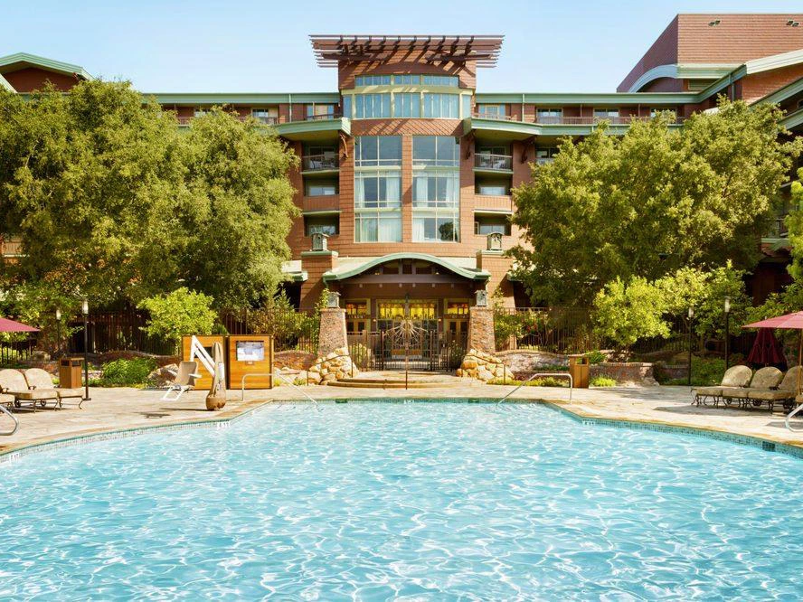 Large swimming pool in front of a multi-story resort with craftsman-style architecture and trees.