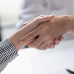 Two people shaking hands over a desk with paperwork, symbolizing a right of first refusal agreement.