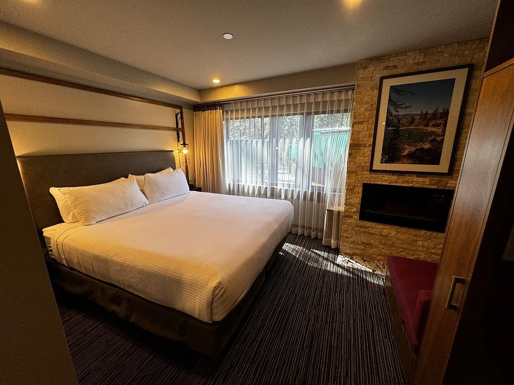 Contemporary resort bedroom featuring a plush king bed, stone fireplace, and large window.