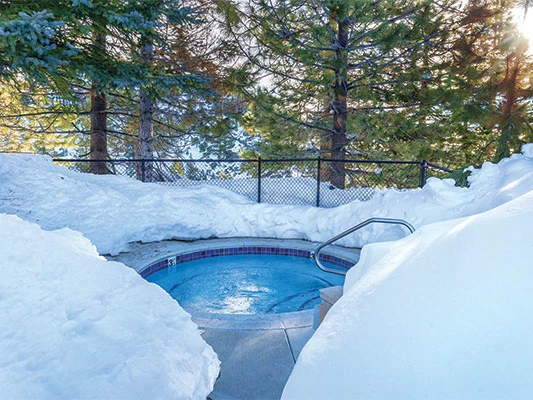 Outdoor circular hot tub surrounded by deep snow and evergreen trees at a Lake Tahoe timeshare.