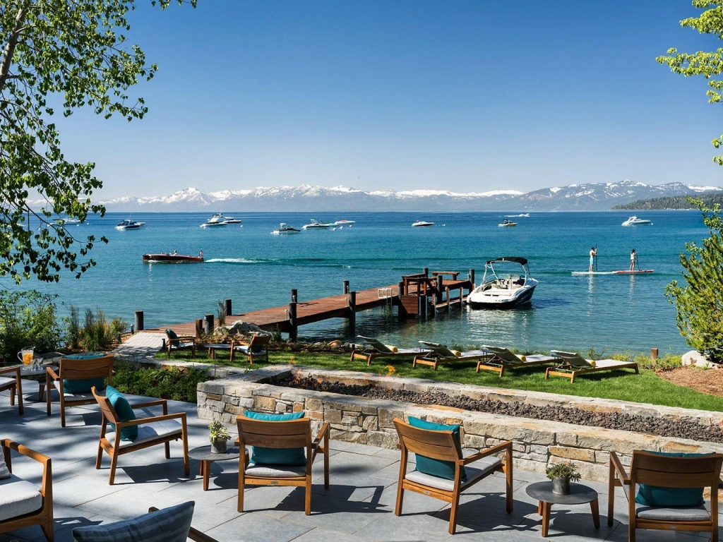 Sunny lakeside patio with wood chairs and a stone fire pit overlooking a pier on Lake Tahoe.