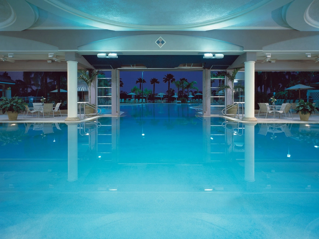 Large indoor-outdoor swimming pool with white pillars reflecting blue water at night at The Fountains.