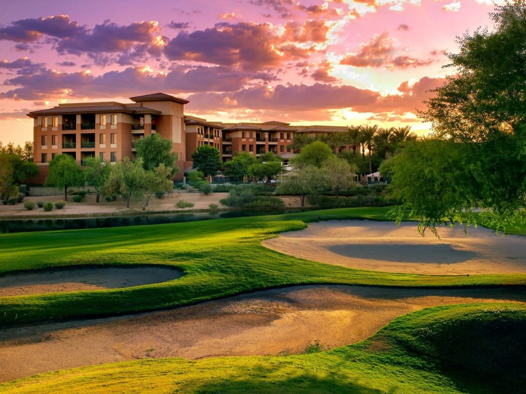 Large resort complex viewed across a lush green golf course with sand traps at sunset.