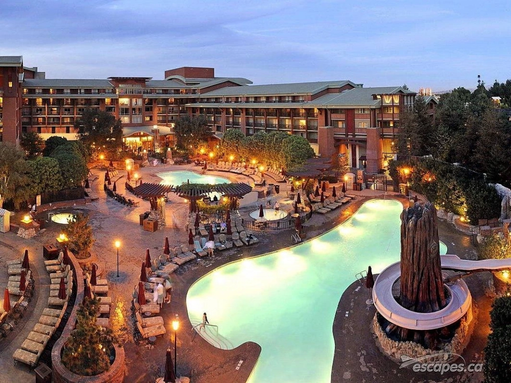 Illuminated swimming pool and redwood tree-themed waterslide at Disney's Grand Californian Hotel at dusk.
