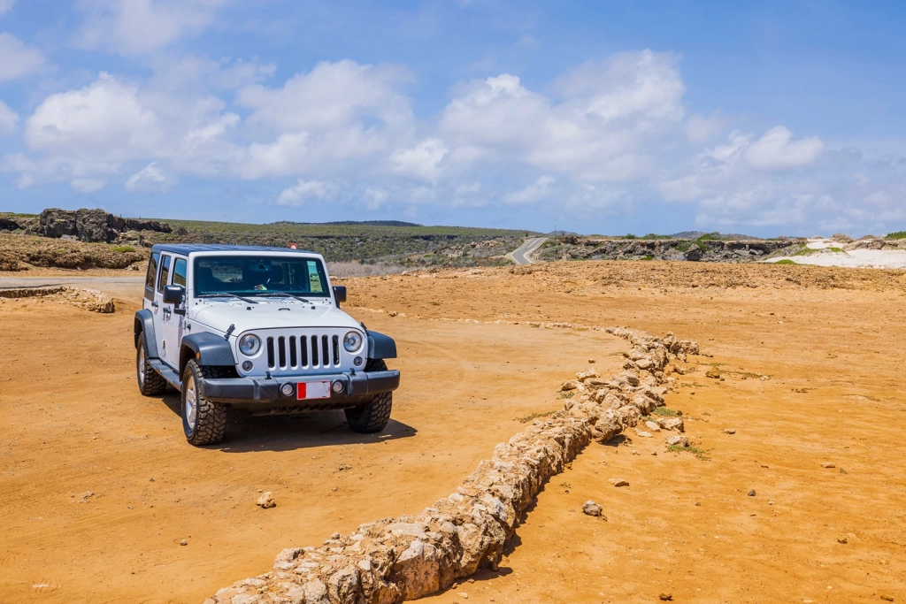 White Jeep Wrangler parked on a rugged, arid dirt trail under a blue sky in Aruba.