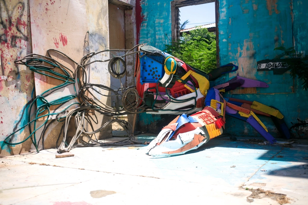 A colorful crab sculpture made from recycled trash by Bordalo II against a blue wall in San Nicolas, Aruba.