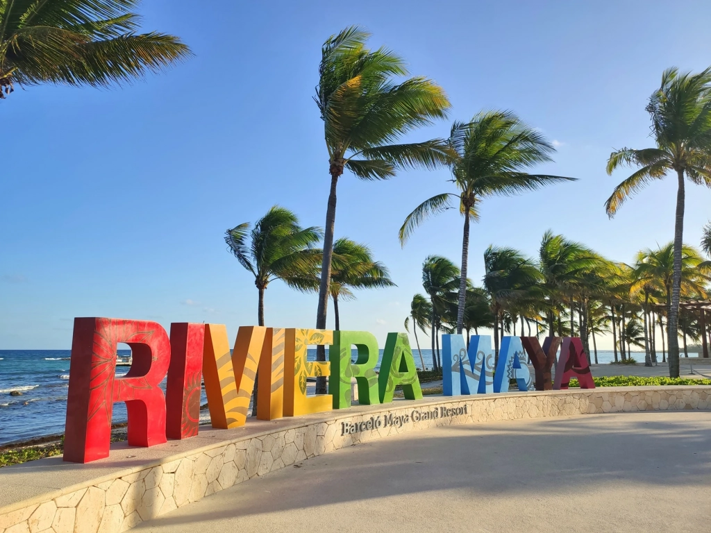 Large, colorful Riviera Maya letters on a stone pathway lined with palm trees near a caribbean timeshare.