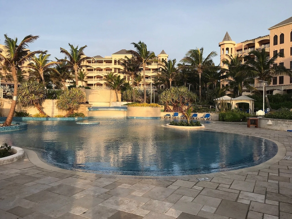 Large, winding swimming pool surrounded by palm trees and resort buildings at a Caribbean timeshare at dusk.