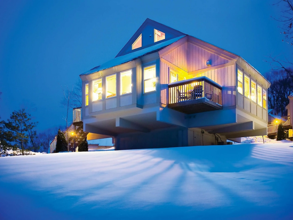 Snow-covered Christmas Mountain Village cabin glowing under a blue night sky.