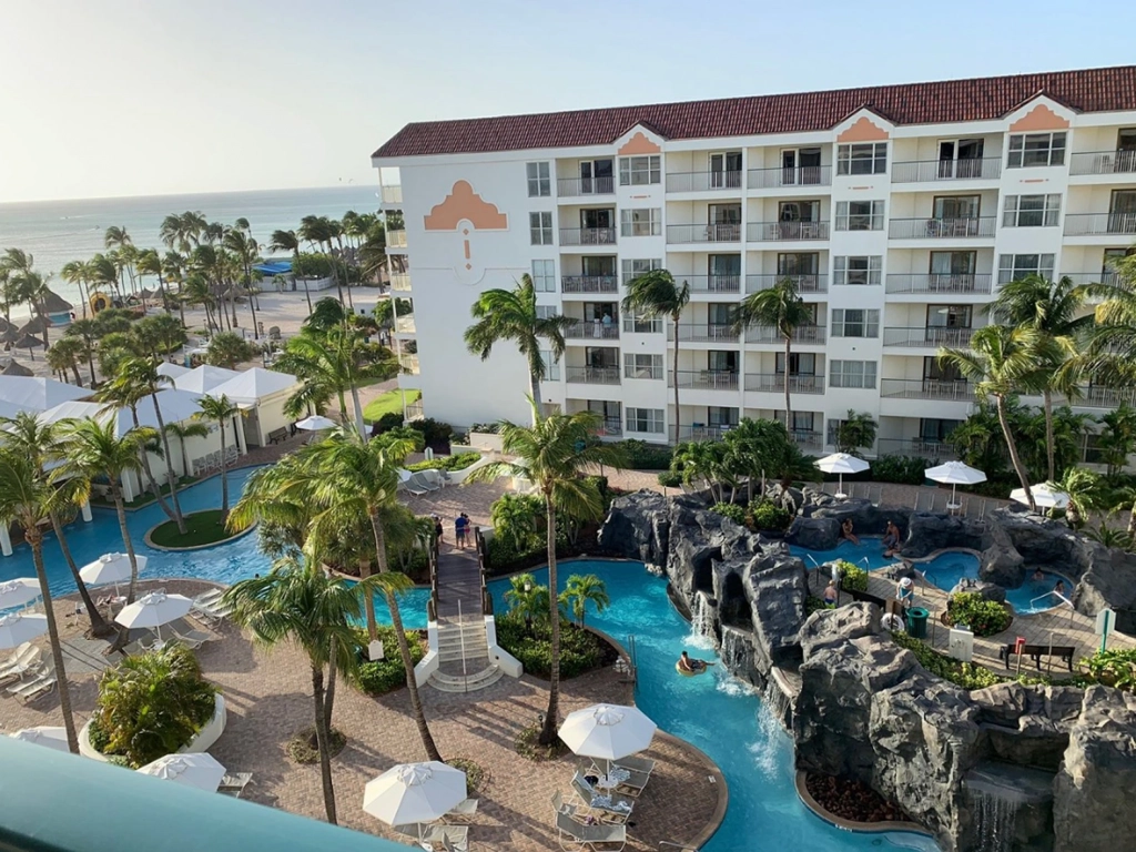 Aerial view of a large meandering pool with rocky waterfall features at the marriott aruba resort, surrounded by palms.