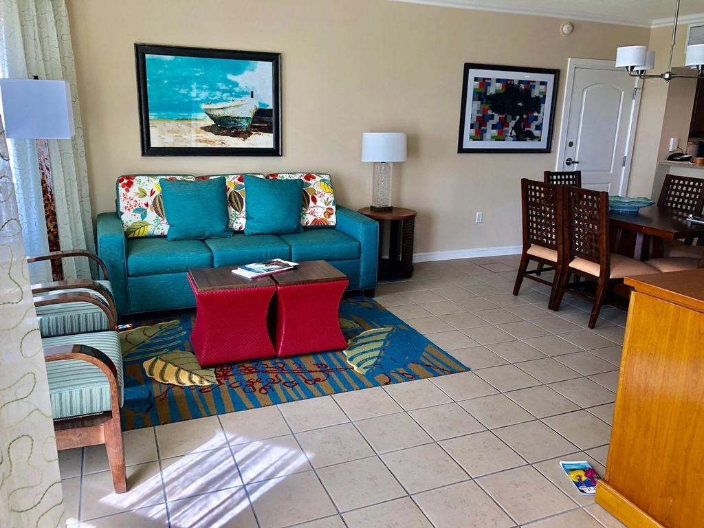 A bright and colorful living room at the marriott aruba resort with a teal couch, red stools, and a dining table.