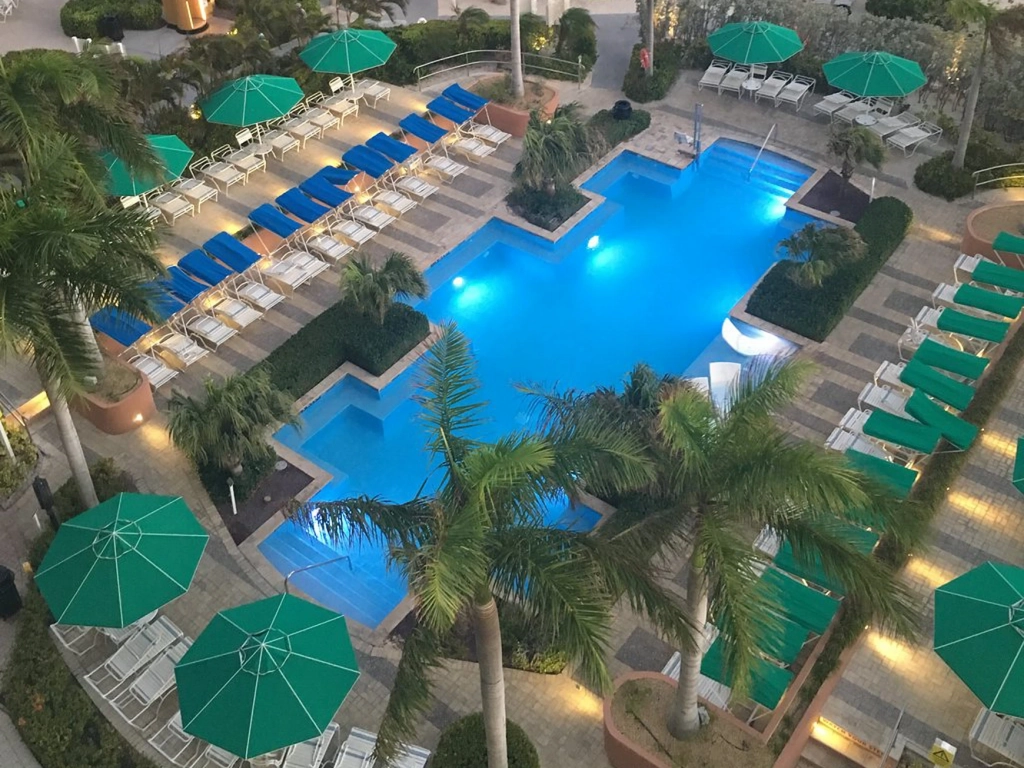 Looking down at a brightly lit swimming pool surrounded by green umbrellas and lounge chairs at the marriott aruba resort.