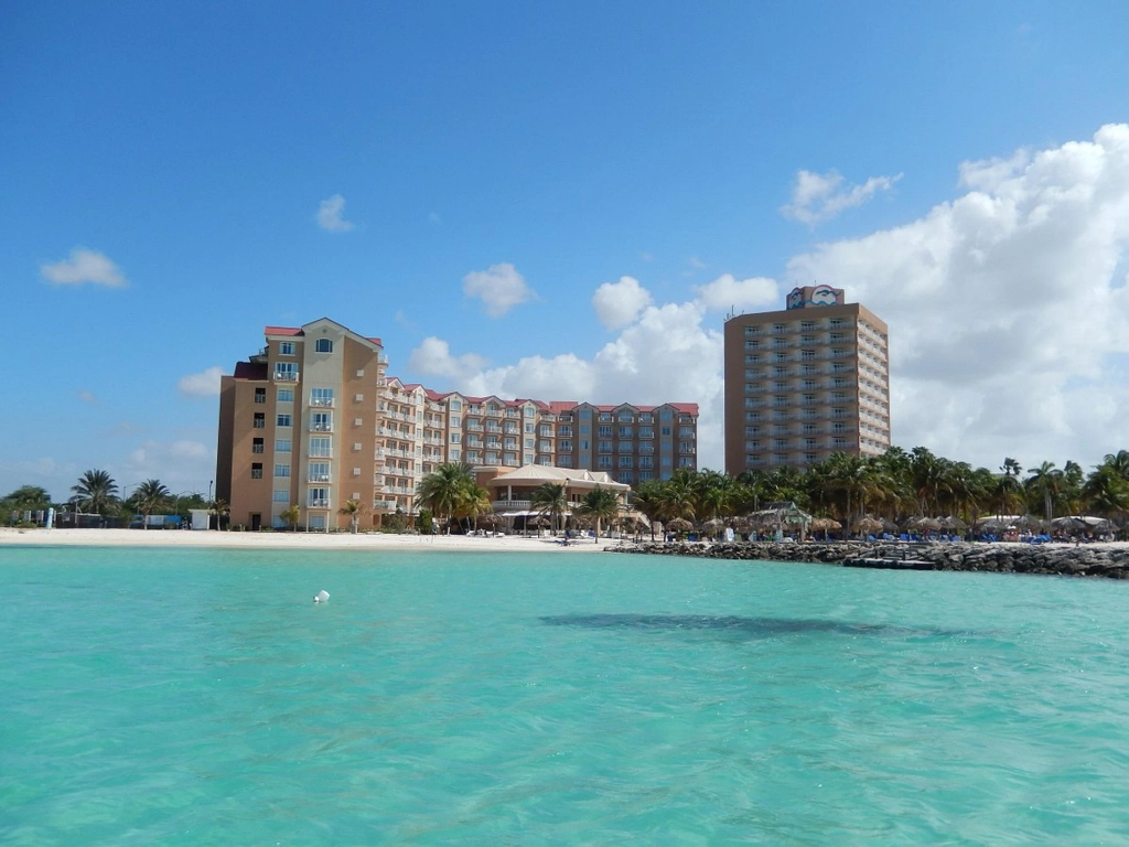 Wide view from the water of a beachfront Caribbean timeshare resort with high-rise buildings and white sand.