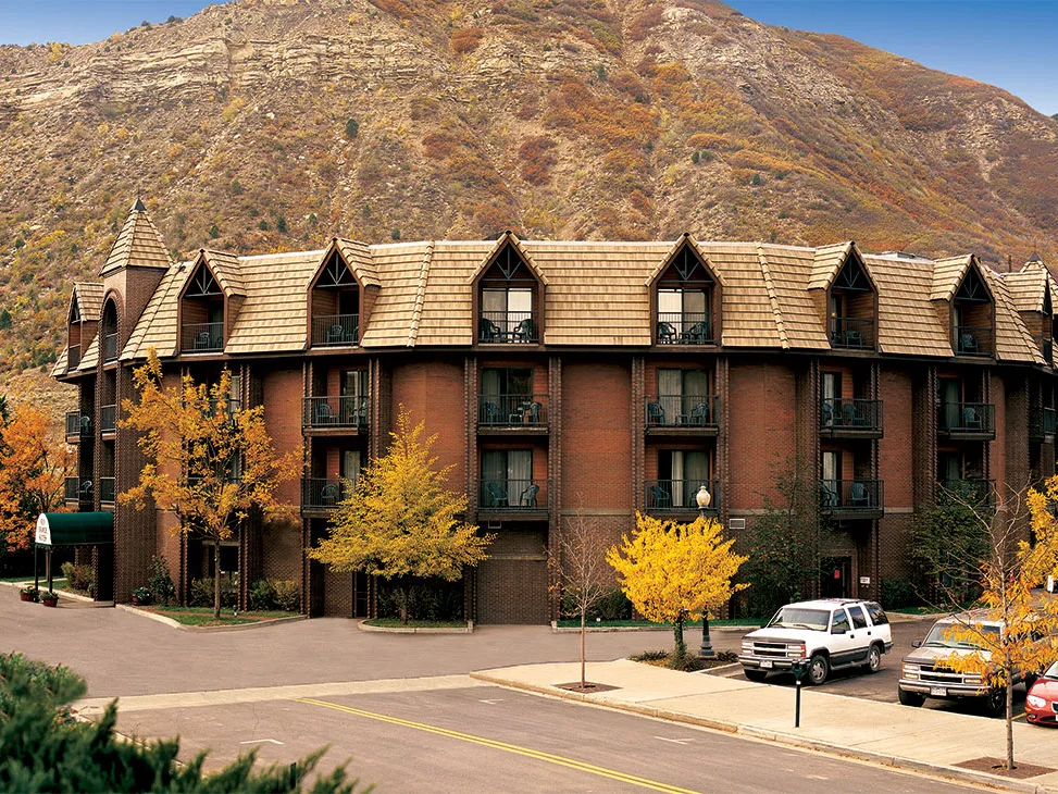 Multi-story brick hotel with gothic dormer roofline and balconies set against an autumn mountain backdrop.