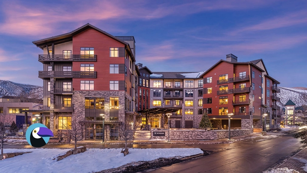 Wyndham hotel exterior at dusk in a snowy mountain setting with warm glowing windows and stone facade.